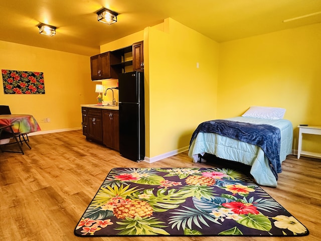 bedroom featuring black fridge, sink, connected bathroom, and light hardwood / wood-style flooring