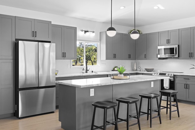 kitchen featuring a center island, hanging light fixtures, sink, appliances with stainless steel finishes, and light stone counters