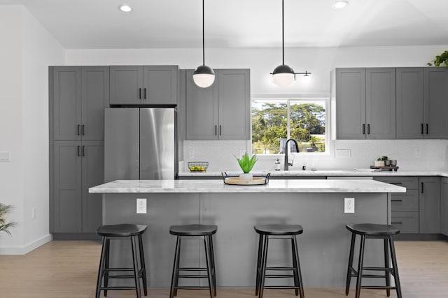 kitchen with stainless steel fridge, gray cabinetry, a breakfast bar, sink, and a kitchen island