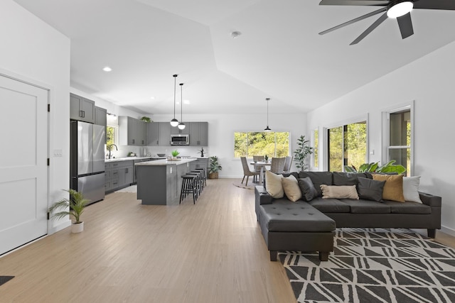 living room with ceiling fan, light wood-type flooring, and lofted ceiling