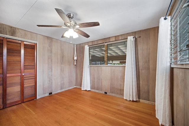 unfurnished bedroom with ceiling fan, light hardwood / wood-style floors, wooden walls, and a closet