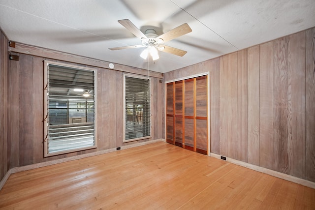 empty room with light wood-type flooring, ceiling fan, and wood walls