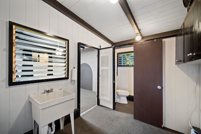 bathroom featuring sink, lofted ceiling with beams, toilet, and wood walls