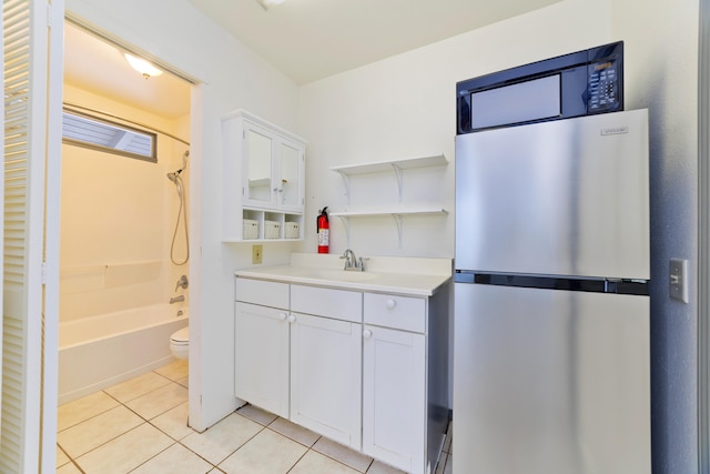 kitchen with light tile patterned flooring, white cabinetry, stainless steel fridge, and sink