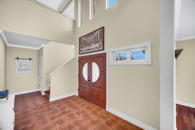 entryway featuring tile patterned flooring, ornamental molding, and a high ceiling