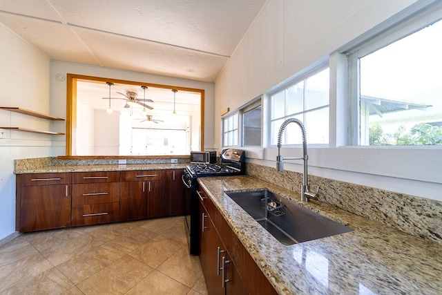 kitchen featuring light tile patterned flooring, range with gas stovetop, sink, ceiling fan, and light stone counters