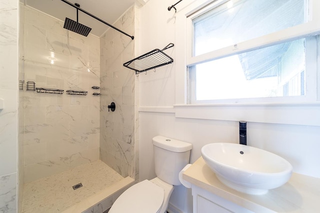 bathroom with a tile shower, vanity, a wealth of natural light, and toilet