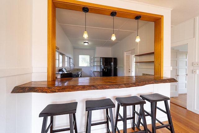 kitchen with decorative light fixtures, wooden counters, a kitchen breakfast bar, kitchen peninsula, and black refrigerator with ice dispenser