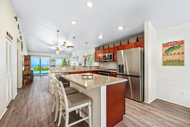 kitchen with kitchen peninsula, light stone counters, stainless steel appliances, decorative light fixtures, and a breakfast bar area