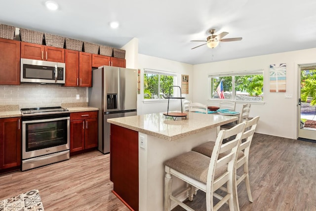 kitchen featuring backsplash, a breakfast bar, stainless steel appliances, ceiling fan, and light hardwood / wood-style flooring