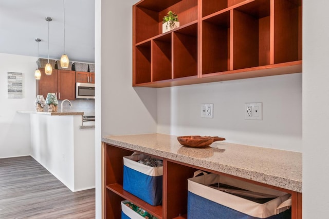 kitchen featuring pendant lighting, backsplash, light hardwood / wood-style flooring, and light stone counters