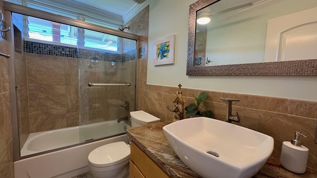 full bathroom with combined bath / shower with glass door, vanity, toilet, and tile walls