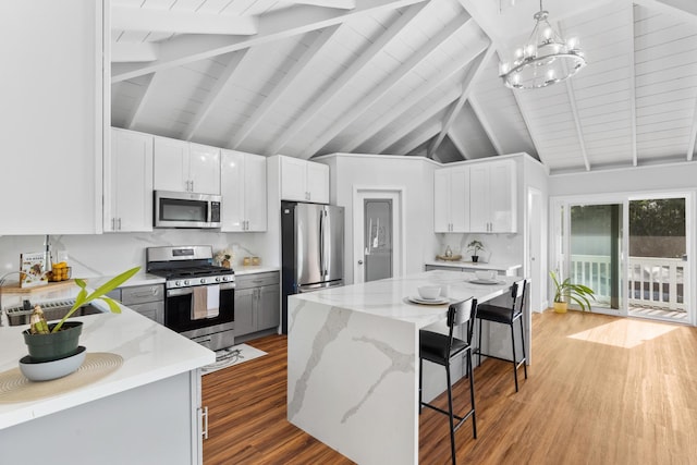 kitchen featuring stainless steel appliances, a center island, white cabinets, and decorative light fixtures