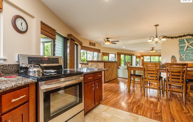 kitchen featuring ceiling fan with notable chandelier, light hardwood / wood-style floors, pendant lighting, and stainless steel electric range oven