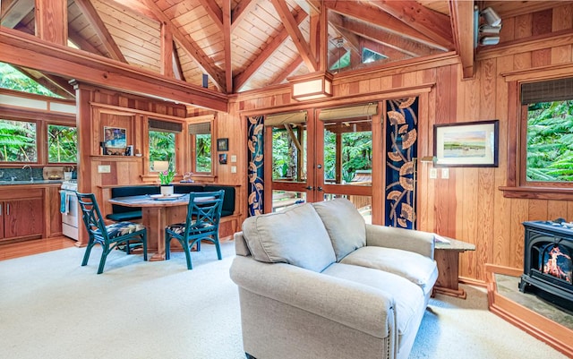 carpeted living area featuring vaulted ceiling with beams, wooden walls, a sink, french doors, and a wood stove