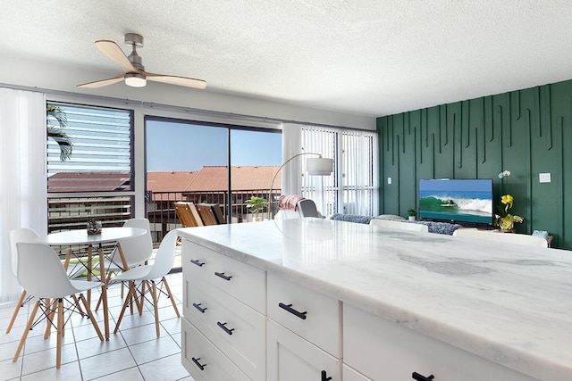 kitchen featuring white cabinets, ceiling fan, light tile patterned floors, a textured ceiling, and light stone counters