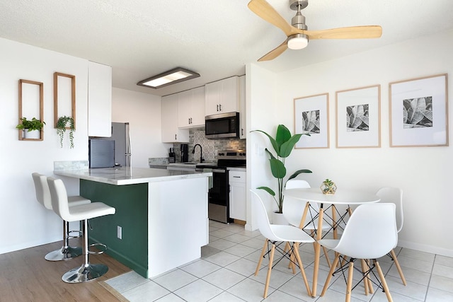 kitchen with backsplash, white cabinets, appliances with stainless steel finishes, a kitchen bar, and kitchen peninsula