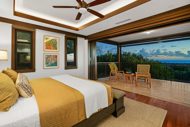 bedroom with hardwood / wood-style flooring, a raised ceiling, access to outside, and ceiling fan