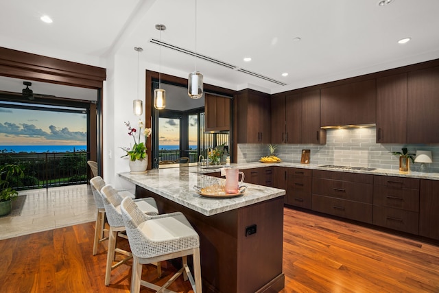 kitchen featuring a breakfast bar, decorative light fixtures, light stone counters, kitchen peninsula, and gas stovetop