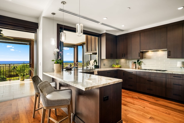 kitchen with light hardwood / wood-style flooring, hanging light fixtures, black gas cooktop, a kitchen bar, and kitchen peninsula