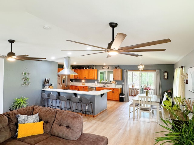 kitchen featuring stainless steel appliances, kitchen peninsula, a breakfast bar area, island range hood, and light wood-type flooring