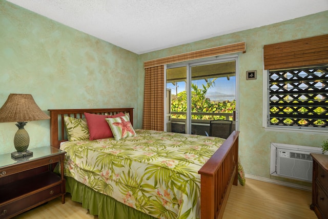 bedroom featuring access to outside, an AC wall unit, a textured ceiling, and light wood-type flooring