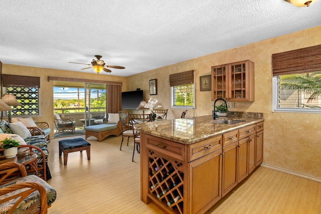 kitchen featuring light stone countertops, ceiling fan, sink, light hardwood / wood-style floors, and a textured ceiling