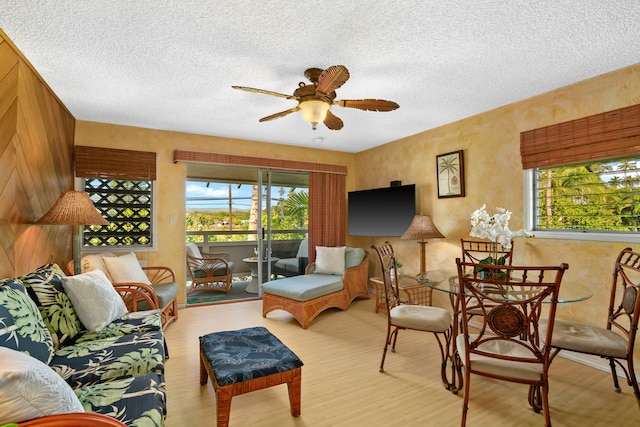 living room with ceiling fan, wood walls, and a textured ceiling