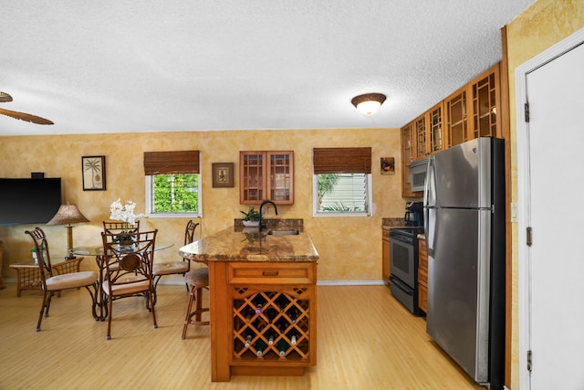 kitchen featuring sink, dark stone countertops, light wood-type flooring, kitchen peninsula, and stainless steel appliances