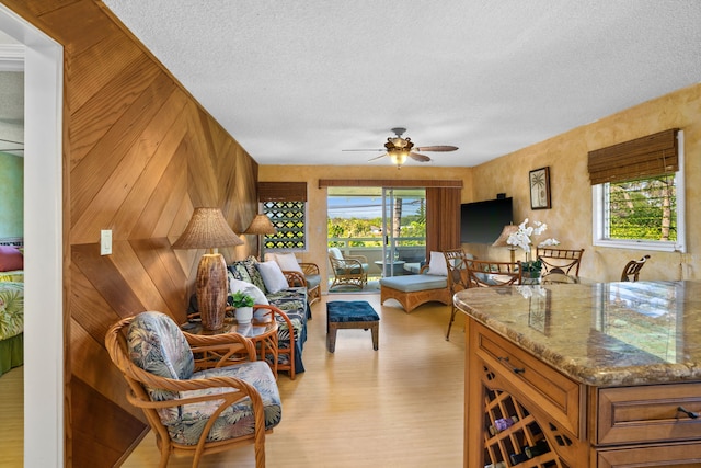 living room with ceiling fan, wood walls, a textured ceiling, and a wealth of natural light