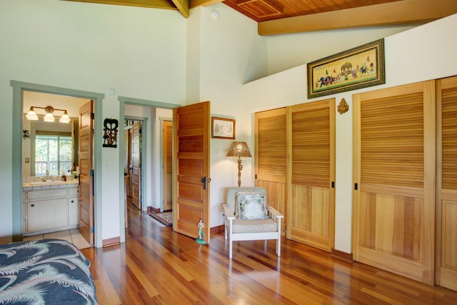 bedroom with hardwood / wood-style floors, vaulted ceiling with beams, two closets, and ensuite bath