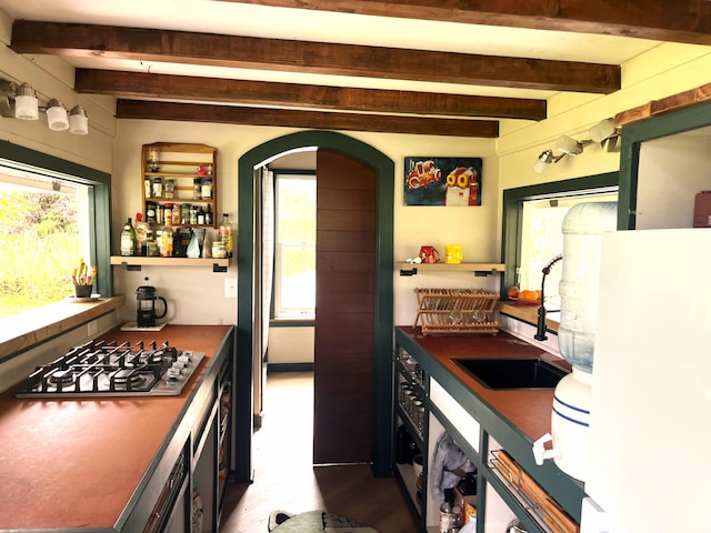 kitchen with stainless steel gas stovetop, arched walkways, beam ceiling, and wood finished floors