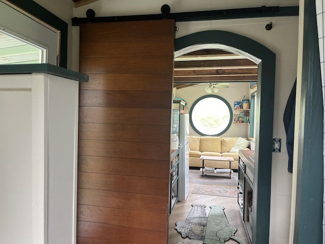 corridor with a barn door, light wood-type flooring, and beam ceiling