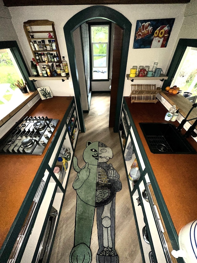 kitchen with arched walkways, a sink, wood finished floors, and stainless steel gas stovetop