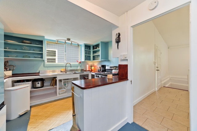 kitchen featuring white cabinetry, sink, light tile patterned flooring, kitchen peninsula, and stainless steel stove