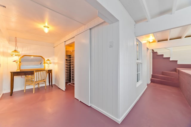 hallway with beam ceiling, concrete flooring, and wooden walls