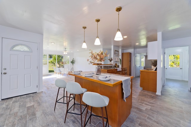 kitchen featuring white cabinets, pendant lighting, a kitchen bar, and light hardwood / wood-style flooring