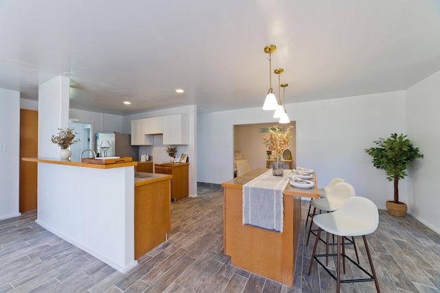 kitchen with stainless steel refrigerator, white cabinetry, a kitchen breakfast bar, kitchen peninsula, and decorative light fixtures