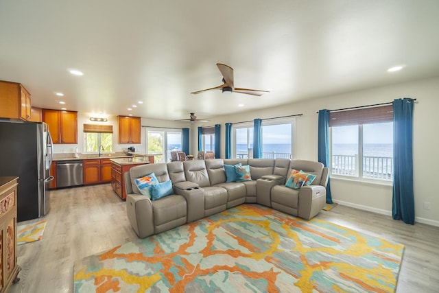 living room featuring ceiling fan, light hardwood / wood-style flooring, a water view, and sink