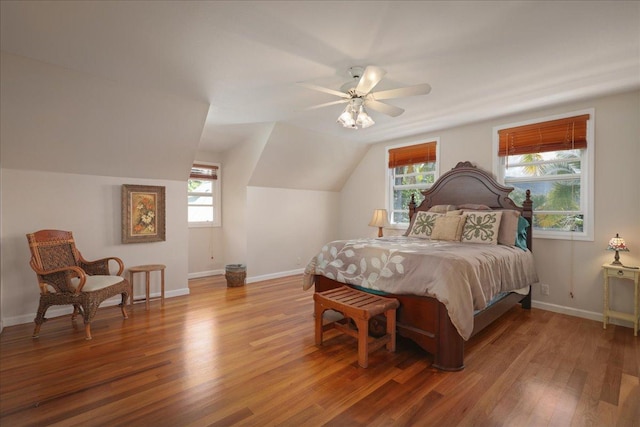 bedroom with multiple windows, ceiling fan, wood-type flooring, and vaulted ceiling