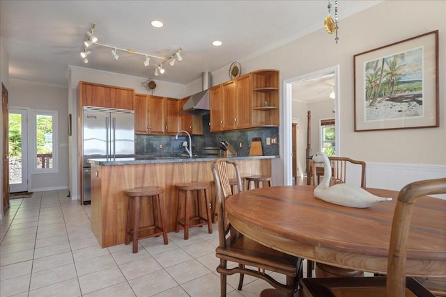 kitchen featuring kitchen peninsula, dark stone counters, crown molding, wall chimney range hood, and light tile patterned floors