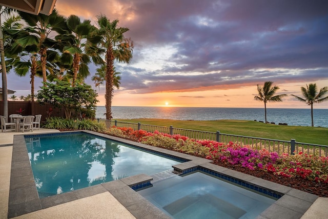 pool at dusk with a water view, a yard, and an in ground hot tub