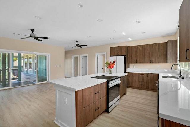 kitchen featuring a center island, brown cabinets, freestanding refrigerator, a sink, and stainless steel electric range