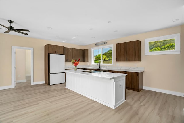 kitchen with light wood finished floors, baseboards, a center island, freestanding refrigerator, and light countertops