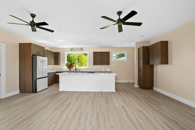 kitchen featuring light wood finished floors, baseboards, a kitchen island, freestanding refrigerator, and light countertops