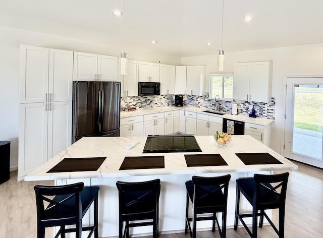 kitchen with pendant lighting, black appliances, sink, a kitchen island, and white cabinetry