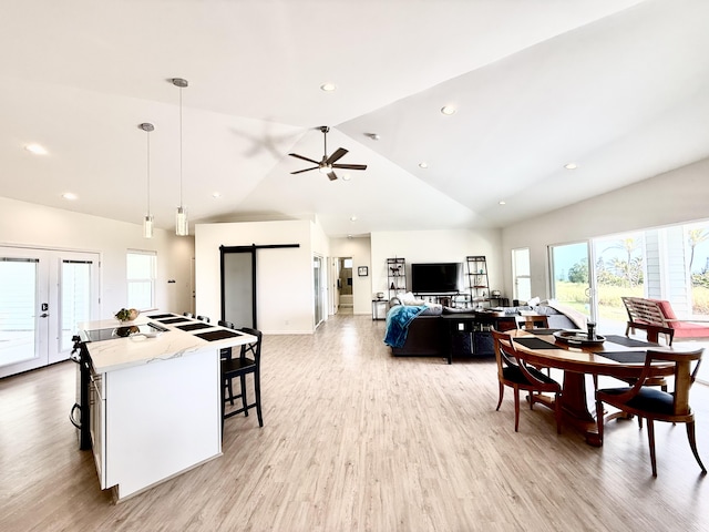 dining space featuring french doors, vaulted ceiling, ceiling fan, a barn door, and light hardwood / wood-style flooring