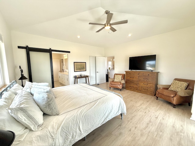 bedroom featuring lofted ceiling, ensuite bathroom, ceiling fan, a barn door, and light wood-type flooring