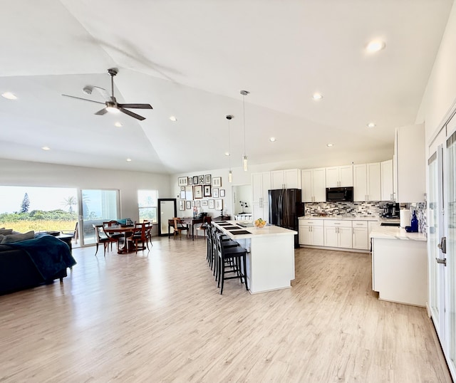 kitchen with a center island, black appliances, hanging light fixtures, vaulted ceiling, and white cabinetry