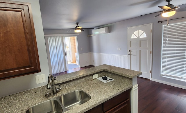 kitchen featuring light stone counters, ceiling fan, sink, an AC wall unit, and dark hardwood / wood-style floors